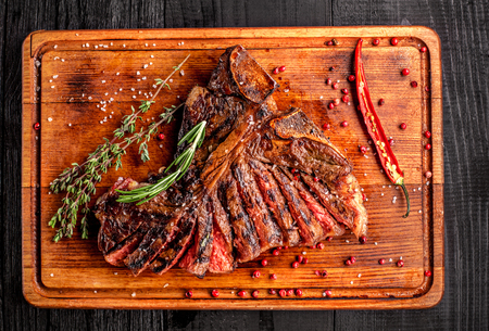 Sliced medium rare grilled steak on rustic cutting board with rosemary and spices , dark rustic wooden background, top viewの写真素材