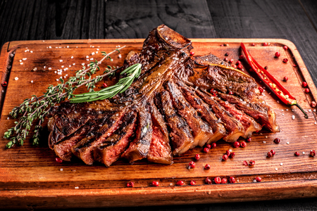 Sliced medium rare grilled steak on rustic cutting board with rosemary and spices , dark rustic wooden background, top viewの写真素材
