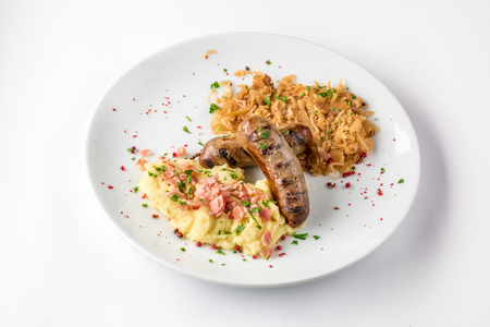 Grilled sausages, potatoes and braised cabbage on white plate close-up view from above.の写真素材