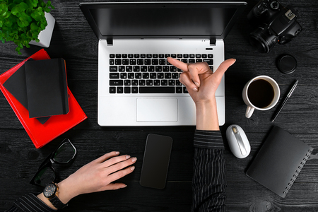 Business and technology topic: the hand of woman in a black shirt showing gesture against background laptop at the desk.の写真素材