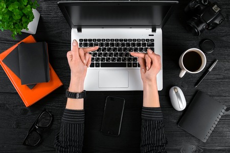 Business and technology topic: the hand of woman in a black shirt showing gesture against background laptop at the desk.の写真素材