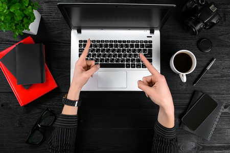 Business and technology topic: the hand of woman in a black shirt showing gesture against background laptop at the desk.の写真素材