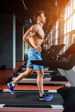 Side view full length of young man in sportswear running on treadmill at gymの写真素材