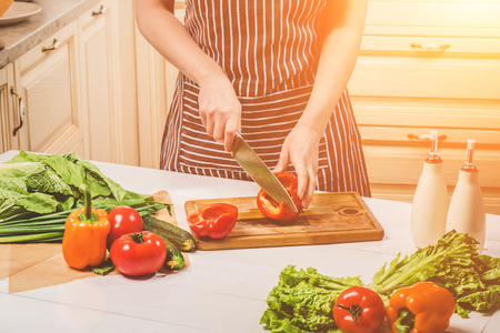 Young woman cooking in the kitchen at home. A woman cuts a pepper and vegetables with a knife.の写真素材