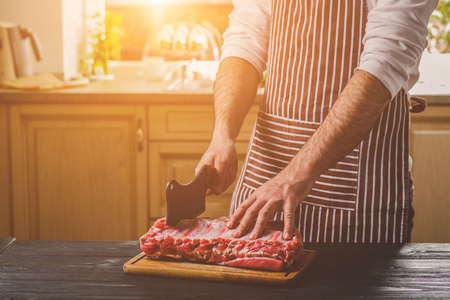 Man cuts of fresh piece of beef on a wooden cutting board in the home kitchenの写真素材