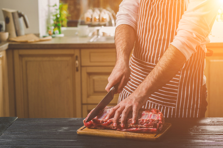 Man cuts of fresh piece of beef on a wooden cutting board in the home kitchenの写真素材