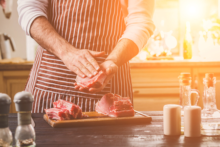 Preparation of dinner. Cooking, processing of meat beef, tenderloin . Person mans hands marinates meat - sprinkles with salt, pepper.の写真素材