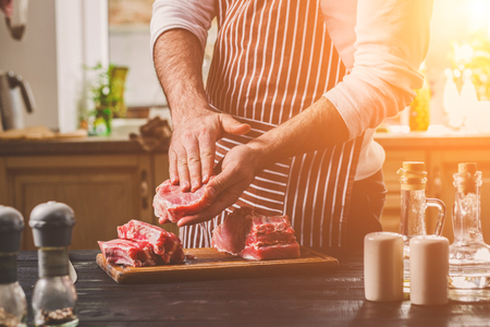 Preparation of dinner. Cooking, processing of meat beef, tenderloin . Person mans hands marinates meat - sprinkles with salt, pepper.の写真素材