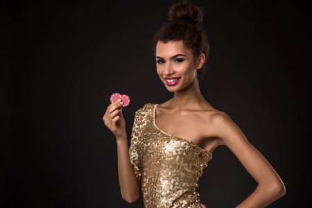 Woman winning - Young woman in a classy gold dress holding two red chips, a poker of aces card combination.の写真素材