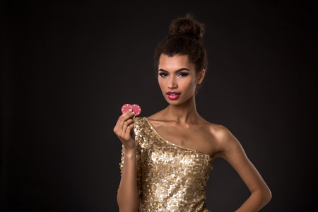 Woman winning - Young woman in a classy gold dress holding two red chips, a poker of aces card combination.の写真素材