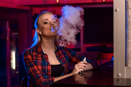 Young pretty woman in a shirt in a cage smoke an electronic cigarette at the vape barの写真素材