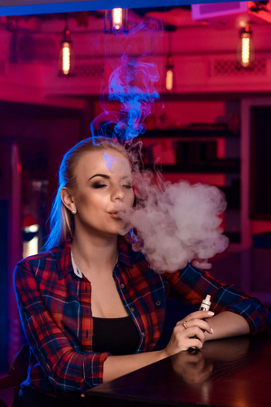 Young pretty woman in a shirt in a cage smoke an electronic cigarette at the vape barの写真素材