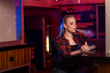 Young pretty woman in a shirt in a cage smoke an electronic cigarette at the vape barの写真素材