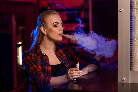 Young pretty woman in a shirt in a cage smoke an electronic cigarette at the vape barの写真素材