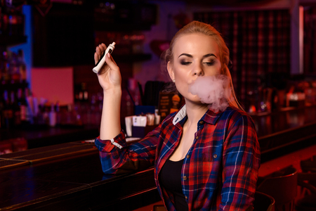 Young pretty woman smoke an electronic cigarette at the vape barの写真素材