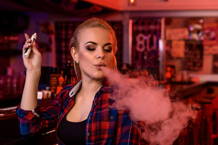 Young pretty woman smoke an electronic cigarette at the vape barの写真素材