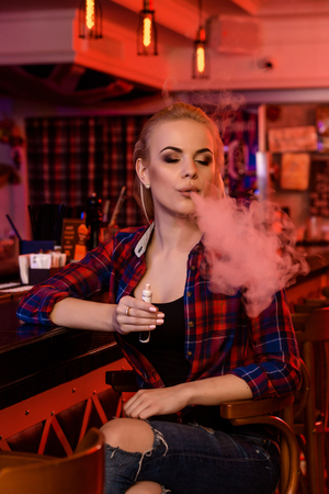 Young pretty woman smoke an electronic cigarette at the vape barの写真素材
