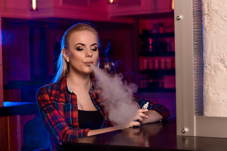 Young pretty woman in a shirt in a cage smoke an electronic cigarette at the vape barの写真素材
