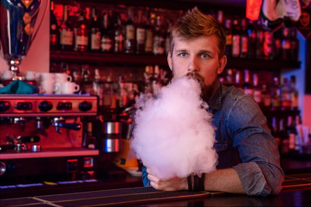 Vape. Vaping man in a cloud of vapor. Photo is taken in a vape bar.の写真素材