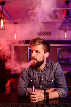 Vape. Vaping man in a cloud of vapor. Photo is taken in a vape bar.の写真素材