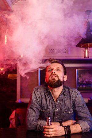 Vape. Vaping man in a cloud of vapor. Photo is taken in a vape bar.の写真素材