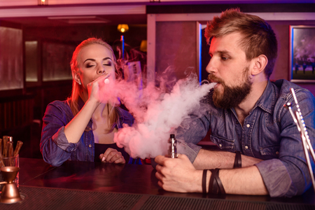 A man and woman smoking electronic cigarette in a vape bar.の写真素材