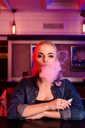 Young pretty woman smoke an electronic cigarette at the vape barの写真素材