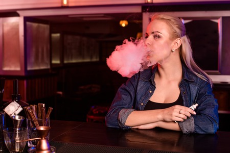Young pretty woman smoke an electronic cigarette at the vape barの写真素材