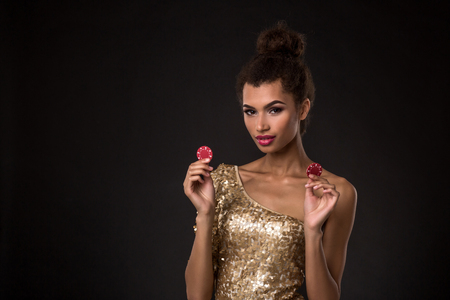 Woman winning - Young woman in a classy gold dress holding two red chips, a poker of aces card combination.の写真素材