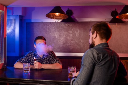 Two young men smoke electronic cigarettes in a vapebarの写真素材
