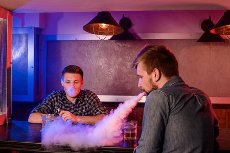 Two young men smoke electronic cigarettes in a vapebarの写真素材