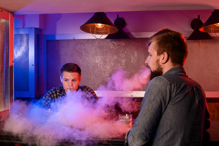 Two young men smoke electronic cigarettes in a vapebarの写真素材