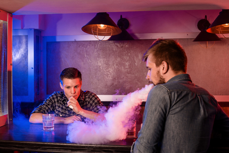 Two young men smoke electronic cigarettes in a vapebarの写真素材