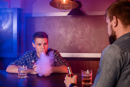 Two young men smoke electronic cigarettes in a vapebarの写真素材