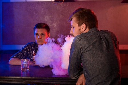 Two young men smoke electronic cigarettes in a vapebarの写真素材