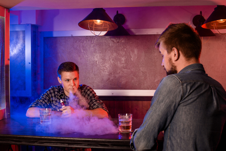 Two young men smoke electronic cigarettes in a vapebarの写真素材