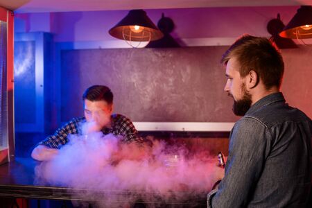 Two young men smoke electronic cigarettes in a vapebarの写真素材