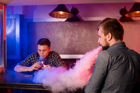 Two young men smoke electronic cigarettes in a vapebarの写真素材