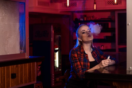 Young pretty woman in a shirt in a cage smoke an electronic cigarette at the vape barの写真素材