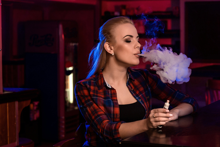 Young pretty woman in a shirt in a cage smoke an electronic cigarette at the vape barの写真素材
