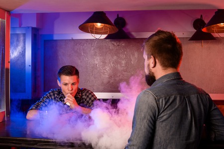 Two young men smoke electronic cigarettes in a vapebar. Vape shopの写真素材