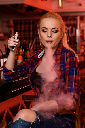 Young pretty woman smoke an electronic cigarette at the vape barの写真素材