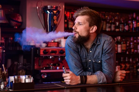Vape. Vaping man in a cloud of vapor. Photo is taken in a vape bar.の写真素材