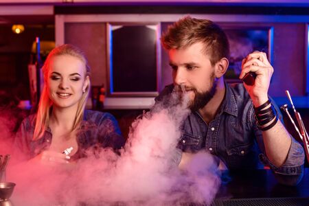 A man and woman smoking electronic cigarette in a vape bar.の写真素材