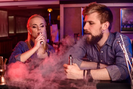 A man and woman smoking electronic cigarette in a vape bar.の写真素材