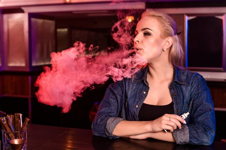 Young pretty woman smoke an electronic cigarette at the vape bar