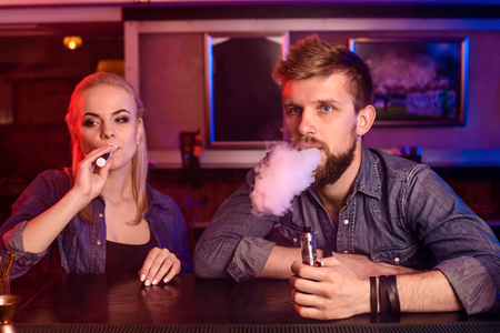 A man and woman smoking electronic cigarette in a vape bar.の写真素材