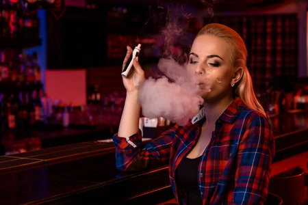 Young pretty woman smoke an electronic cigarette at the vape barの写真素材
