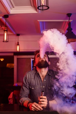 Vape. Vaping man in a cloud of vapor. Photo is taken in a vape bar.の写真素材