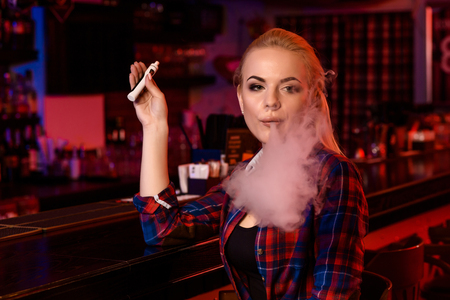 Young pretty woman smoke an electronic cigarette at the vape barの写真素材